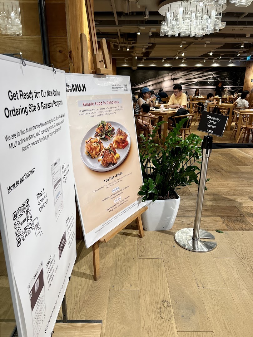 Interior view of CafèMeal MUJI with diners, featuring promotional signs for online ordering and deli sets.