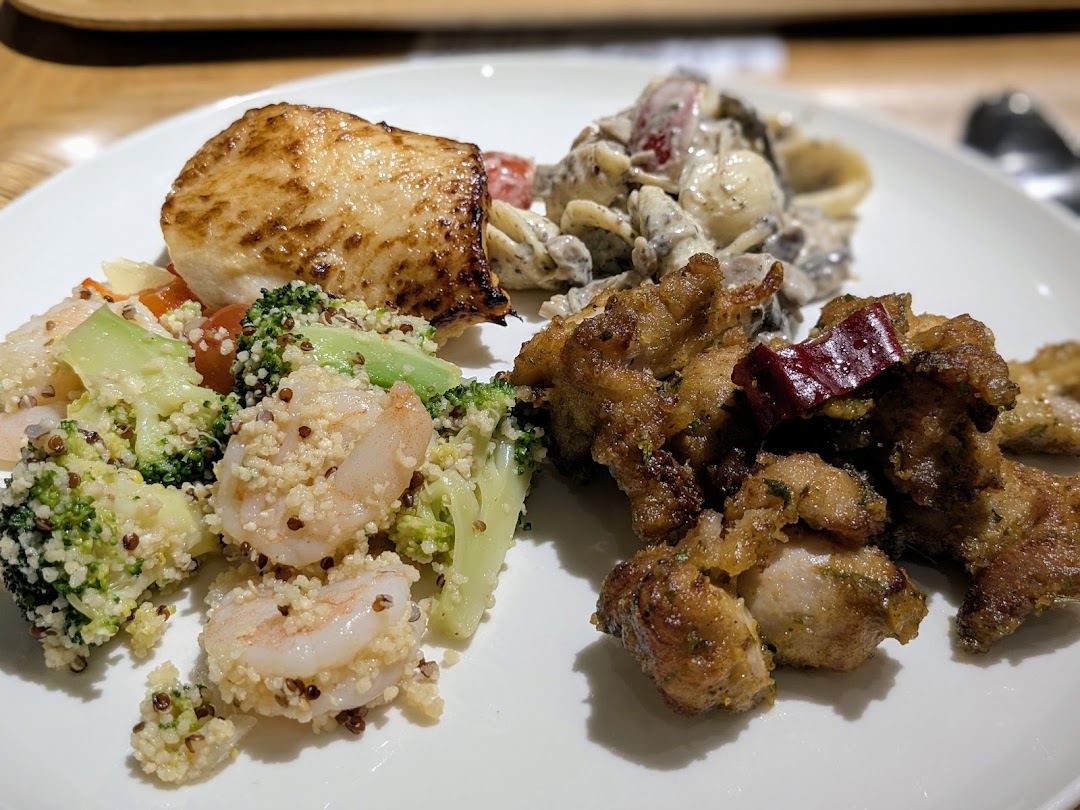 A delicious plate featuring grilled fish, shrimp quinoa salad, pasta, and fried chicken from CafèMeal.