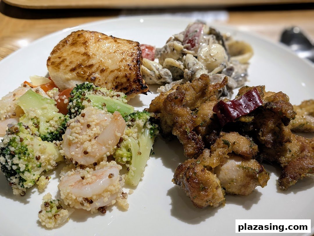 A delicious plate featuring grilled fish, shrimp quinoa salad, pasta, and fried chicken from CafèMeal.