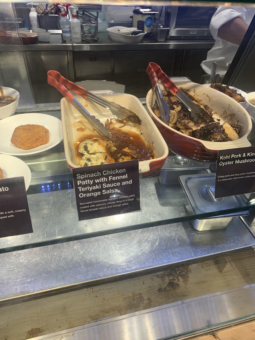 Close-up of prepared food items with descriptive labels in a cafe's hot food display.