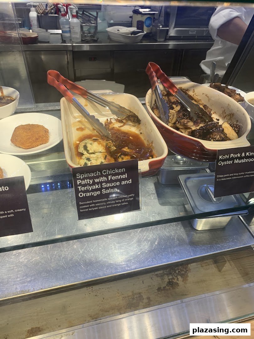 Close-up of prepared food items with descriptive labels in a cafe's hot food display.