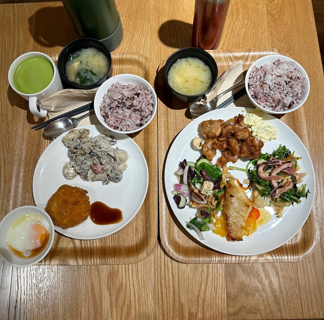 Two trays of Japanese-style meals featuring rice, soup, fried dishes, and fresh salads on a wooden table.