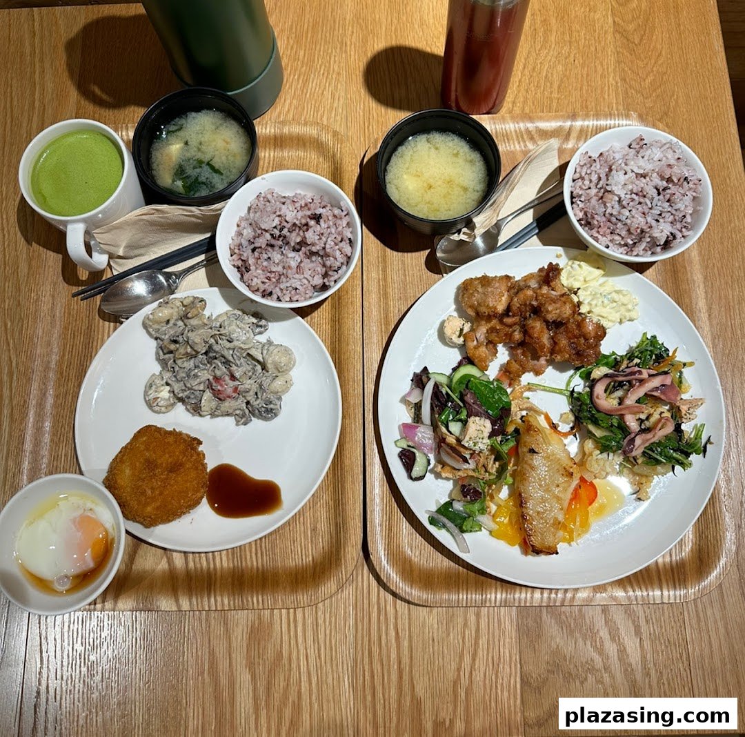 Two trays of Japanese-style meals featuring rice, soup, fried dishes, and fresh salads on a wooden table.
