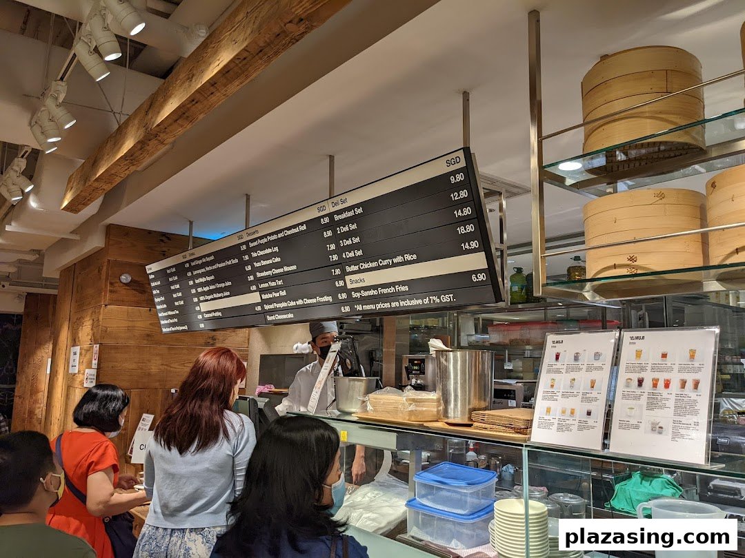 Customers queue at the counter of CafèMeal, featuring a large overhead menu board and display cases.