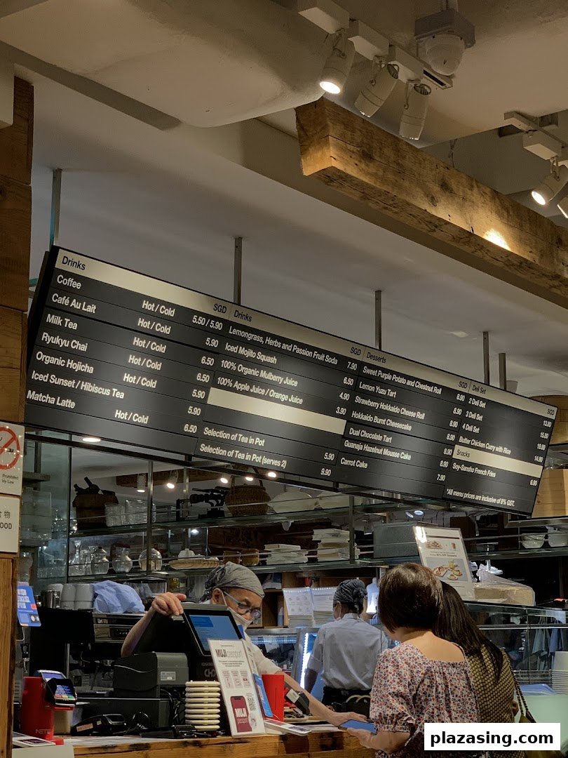 Overhead menu board displaying drinks, desserts, and deli sets at a cafe counter with customers.