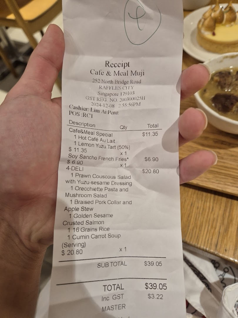 A hand holds a receipt from Cafe & Meal Muji, detailing food and drink purchases.