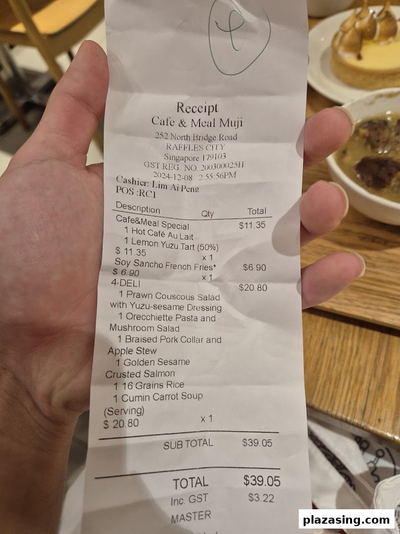 A hand holds a receipt from Cafe & Meal Muji, detailing food and drink purchases.