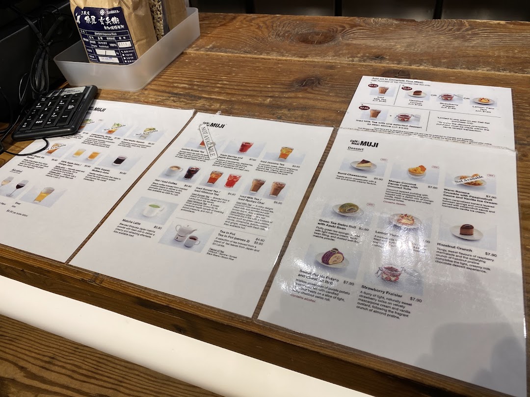 Laminated menu pages displaying drinks, desserts, and meal add-ons on a wooden counter at CafèMeal MUJI.