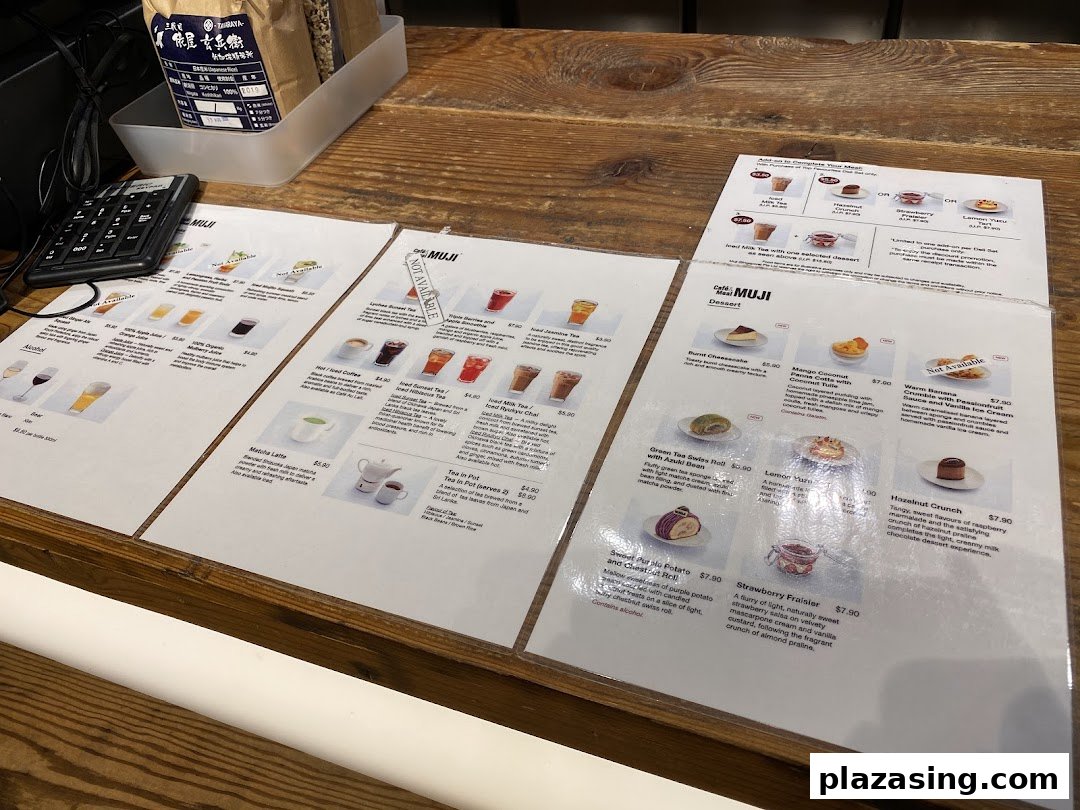 Laminated menu pages displaying drinks, desserts, and meal add-ons on a wooden counter at CafèMeal MUJI.