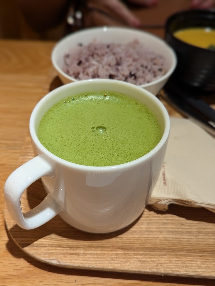 A vibrant green matcha latte in a white mug, served with wholesome rice and soup on a wooden tray.