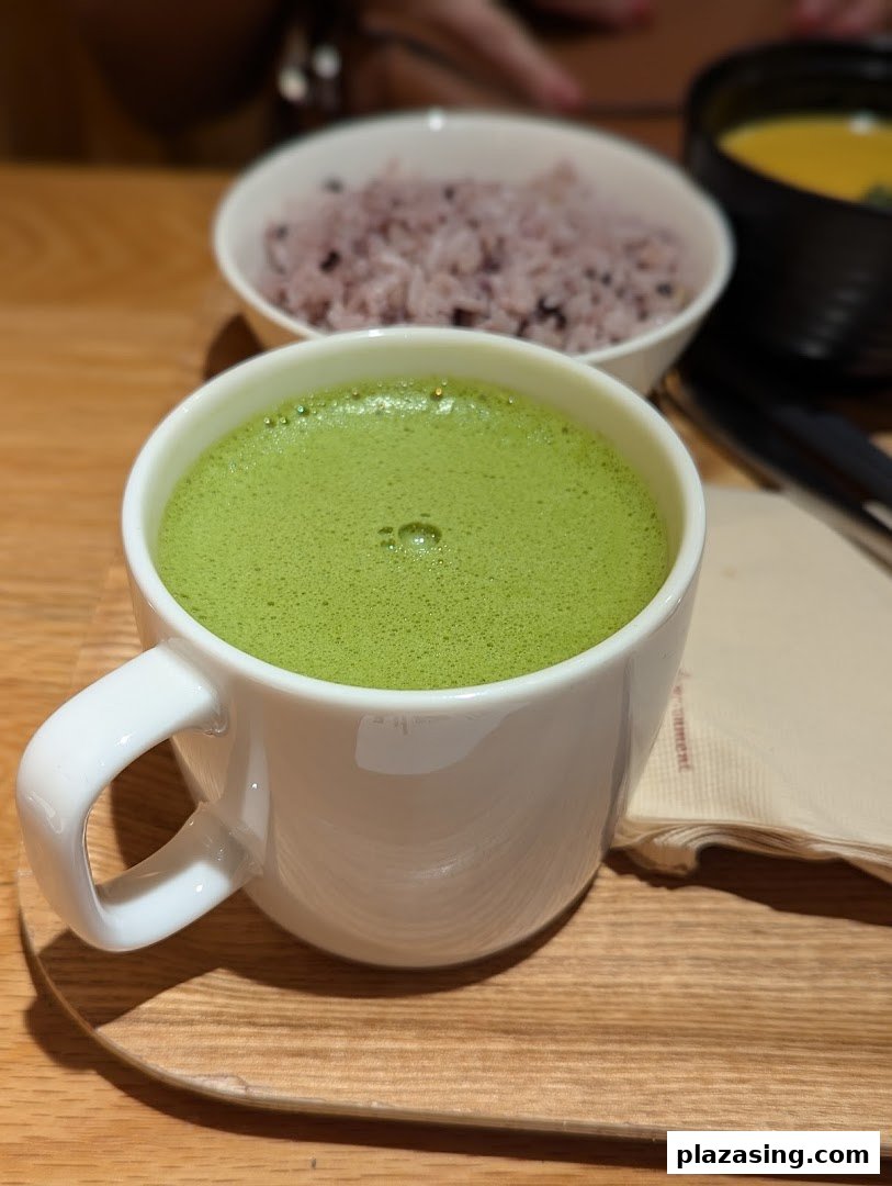 A vibrant green matcha latte in a white mug, served with wholesome rice and soup on a wooden tray.