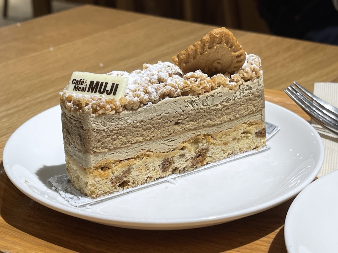 A delicious layered cake with a biscuit topping and 'Café & Meal MUJI' chocolate on a white plate.