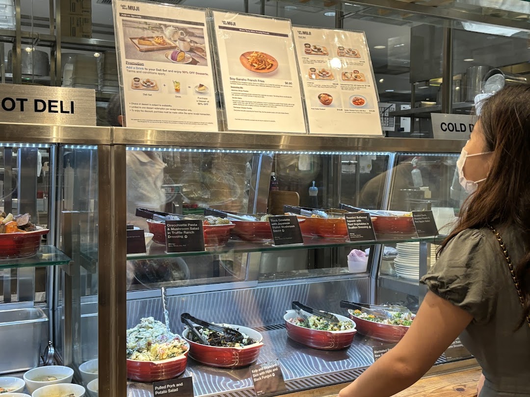 Customer views a deli counter with prepared food and menu boards at CafèMeal MUJI.