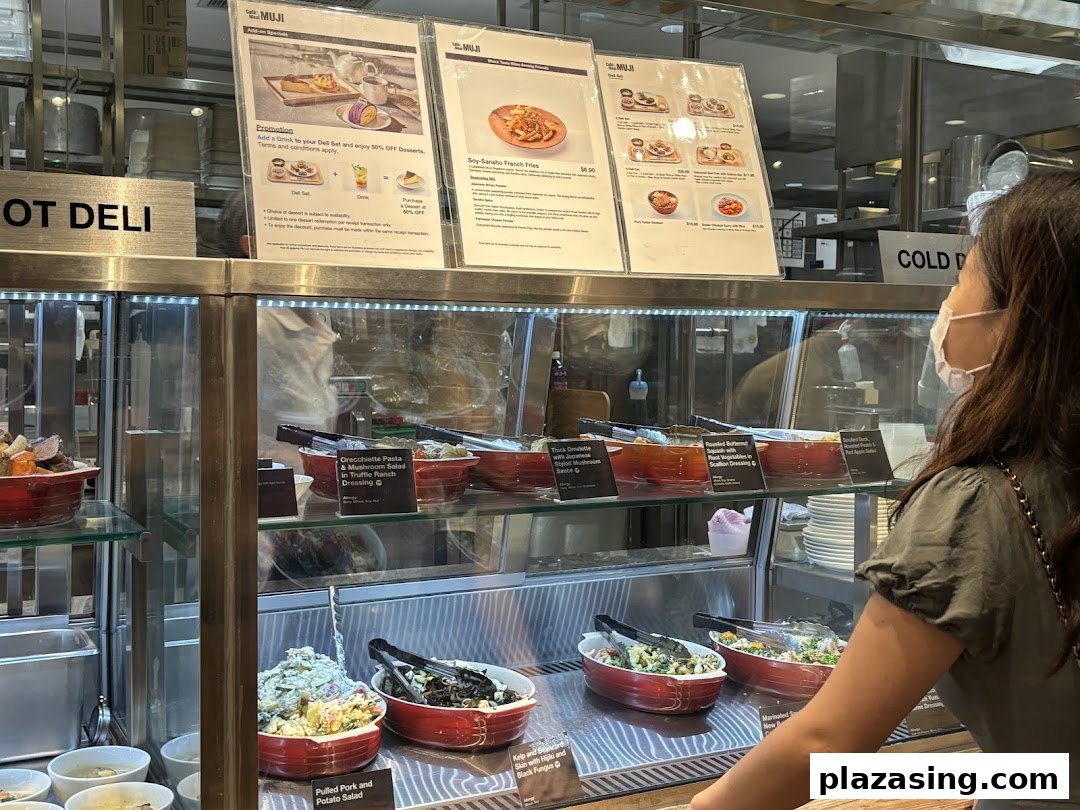 Customer views a deli counter with prepared food and menu boards at CafèMeal MUJI.