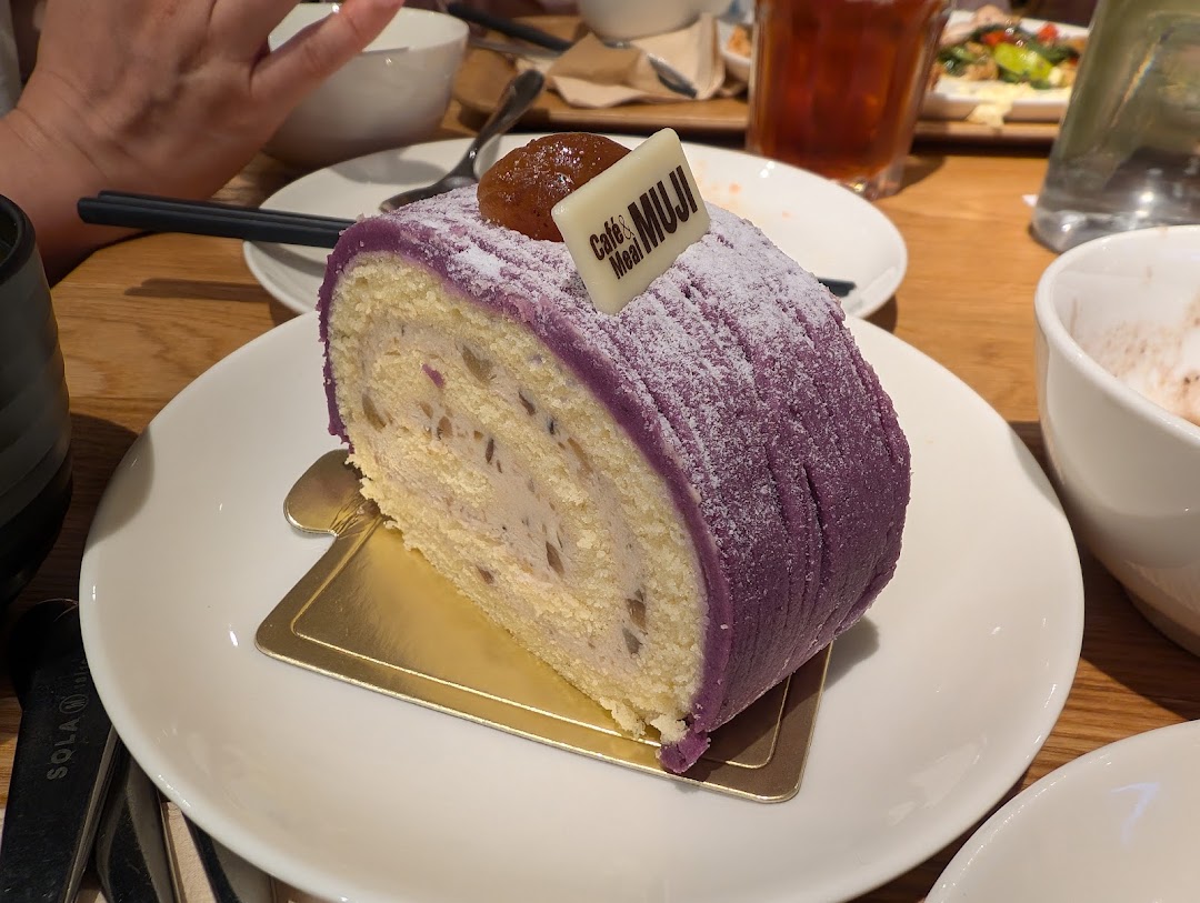 A delicious slice of purple yam roll cake with a "Café&Meal MUJI" tag on a white plate.
