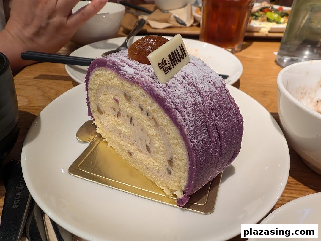A delicious slice of purple yam roll cake with a "Café&Meal MUJI" tag on a white plate.