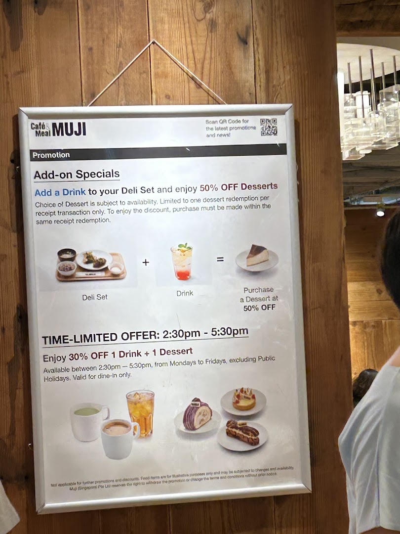 A promotional sign for CafèMeal MUJI displaying special offers on deli sets, drinks, and desserts.