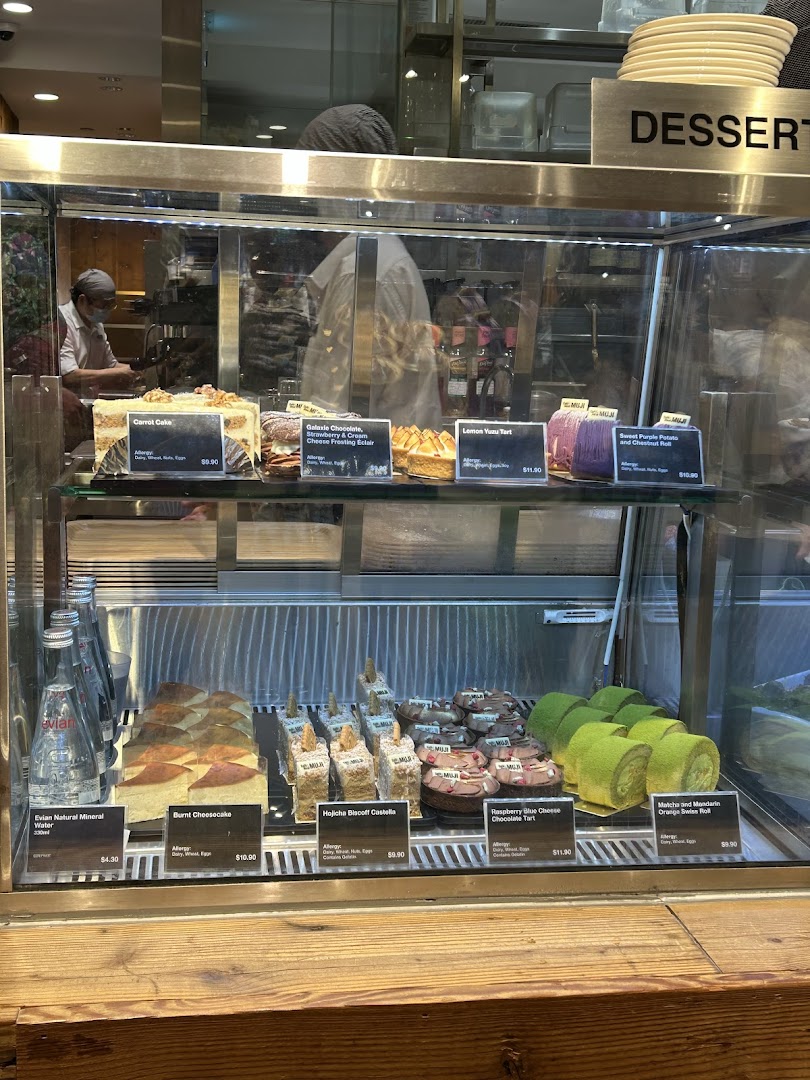 A glass display case showcasing a variety of delicious cakes, tarts, and bottled water.