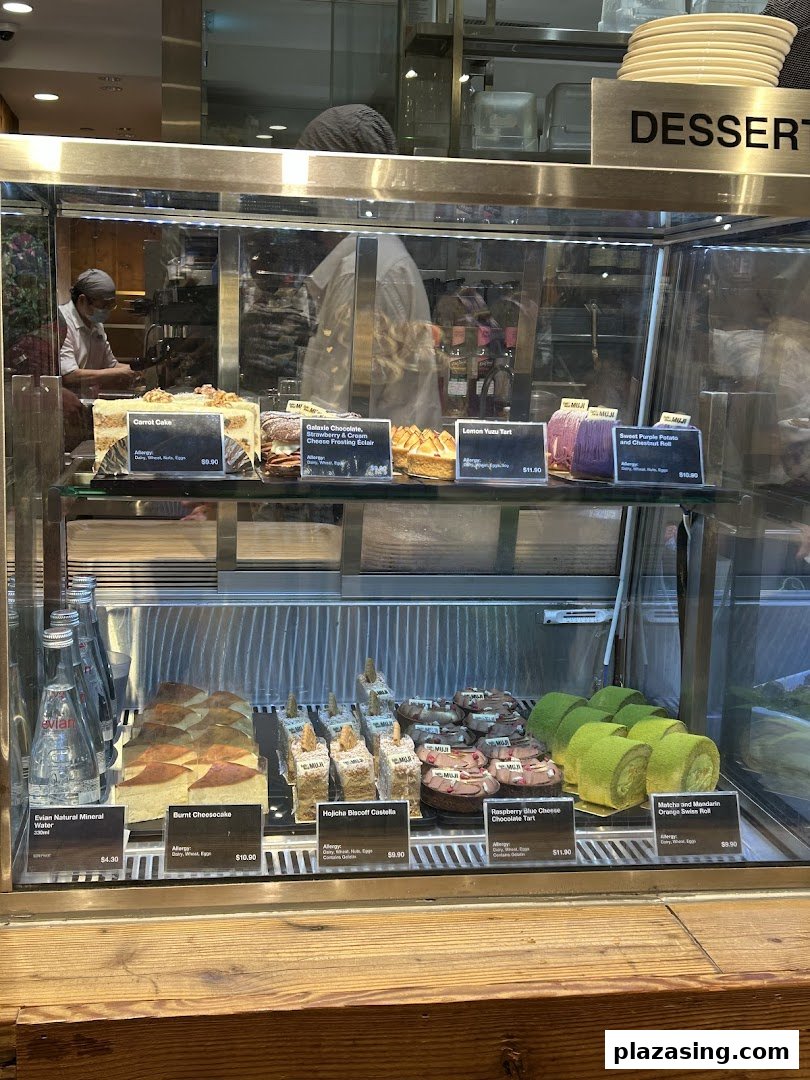 A glass display case showcasing a variety of delicious cakes, tarts, and bottled water.