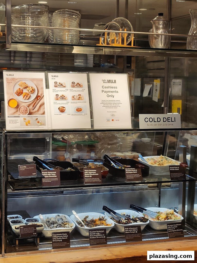 A display case at CafèMeal MUJI showcasing various cold deli dishes and menu boards for set meals.