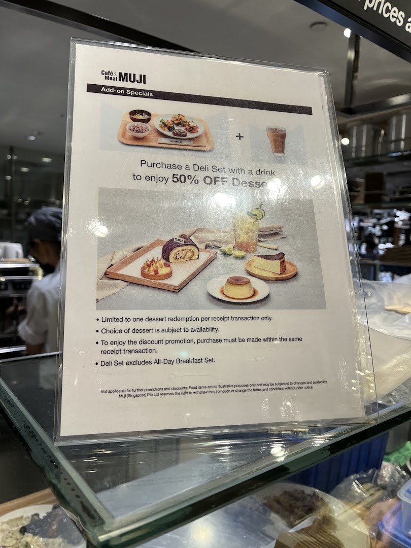 A promotional sign at Cafe&Meal MUJI showcasing a 50% off dessert offer with a deli set purchase.