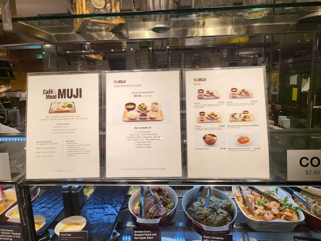 A display case showcasing various deli items and menu boards for breakfast and deli sets at Cafè & Meal MUJI.