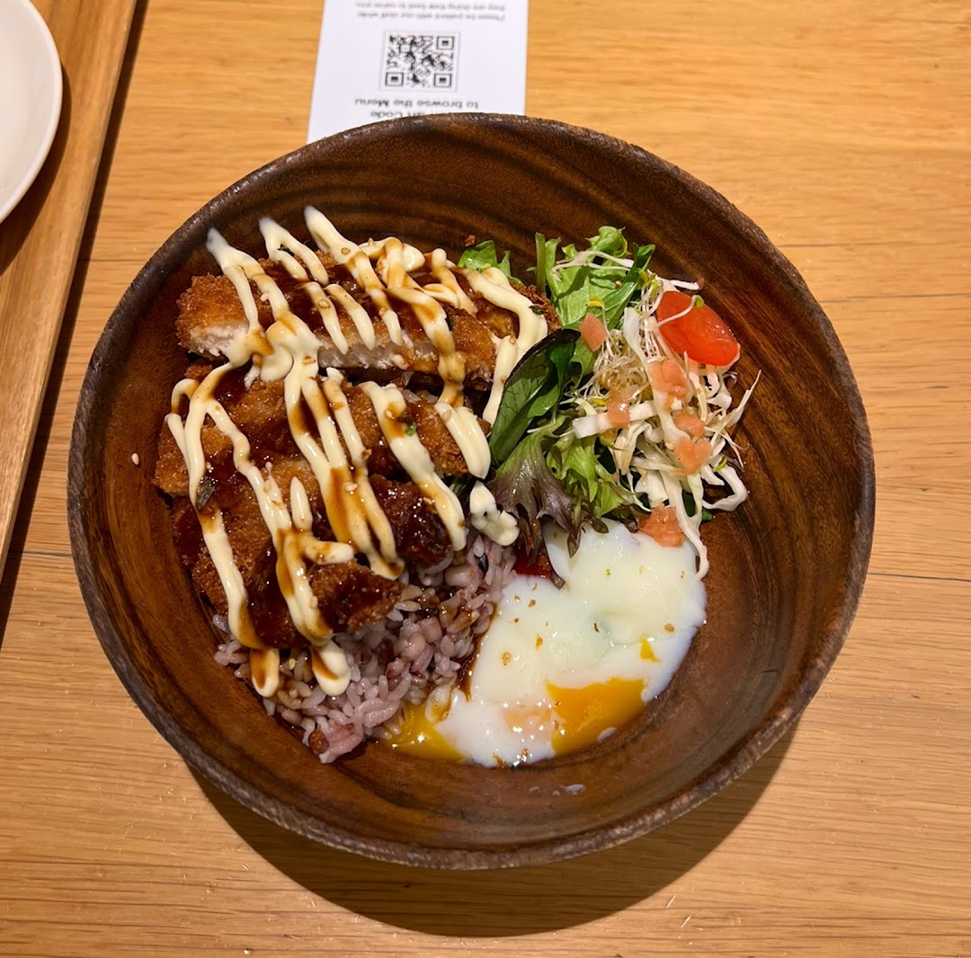 A delicious Japanese-style rice bowl featuring crispy fried chicken, a soft-boiled egg, and fresh salad.