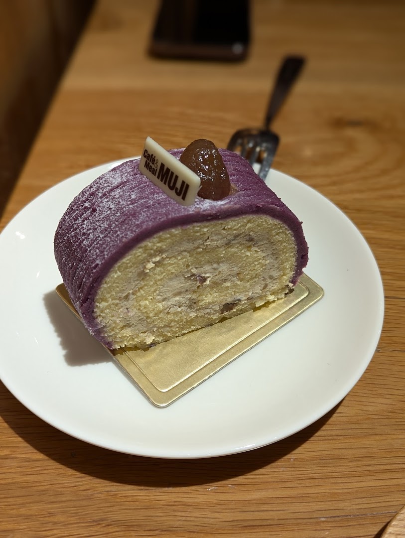 A delicious slice of purple sweet potato roll cake with a Café & Meal MUJI tag on a white plate.