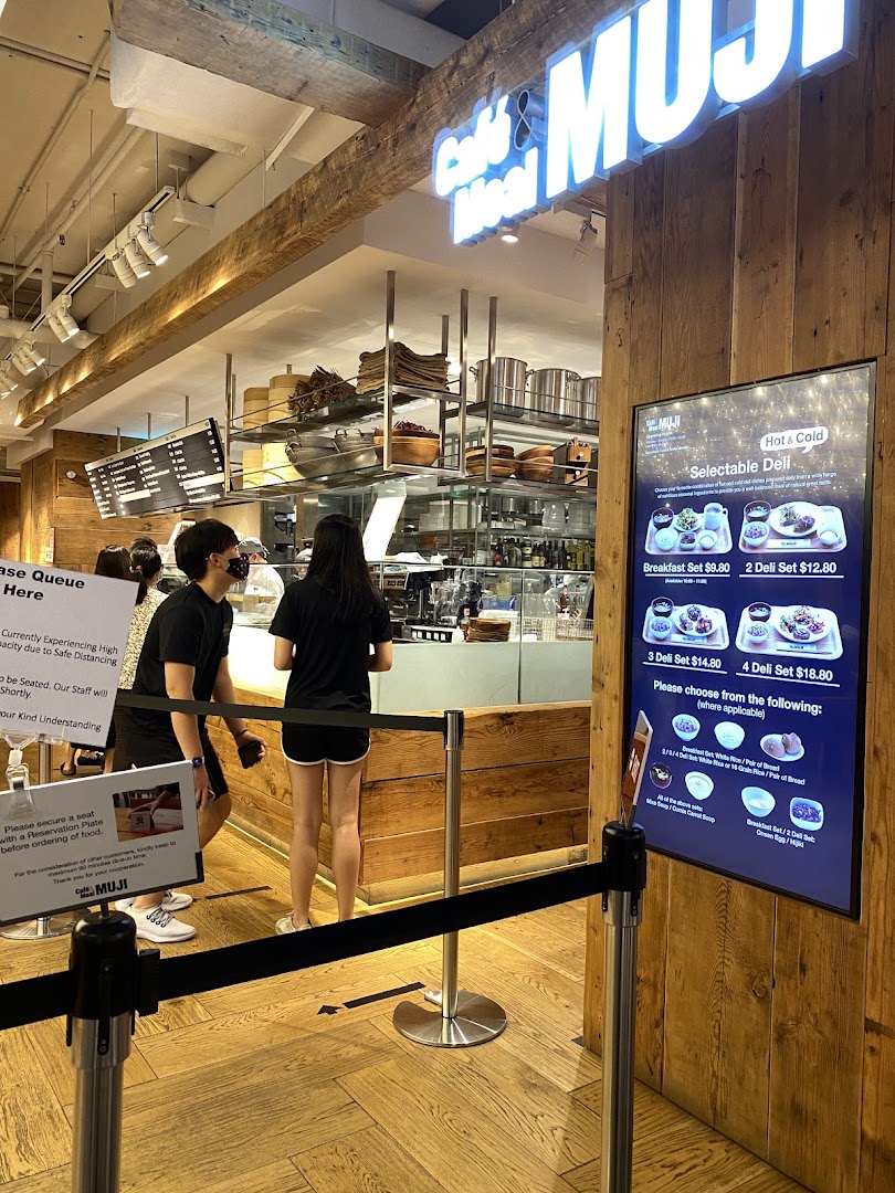Customers queueing at CafèMeal MUJI, with a digital menu board displaying hot and cold selectable deli sets.