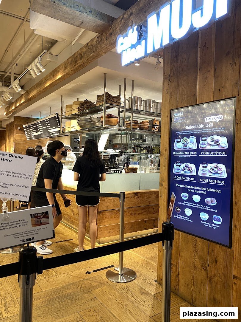 Customers queueing at CafèMeal MUJI, with a digital menu board displaying hot and cold selectable deli sets.
