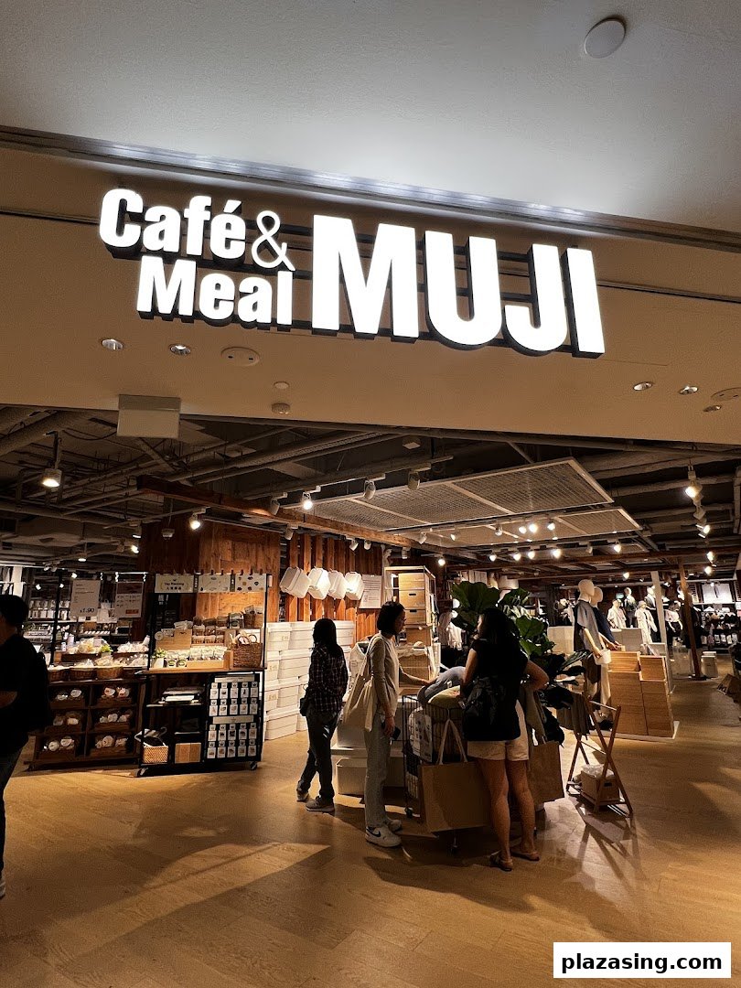 Illuminated 'Café & Meal MUJI' sign above a spacious shop interior with customers browsing.