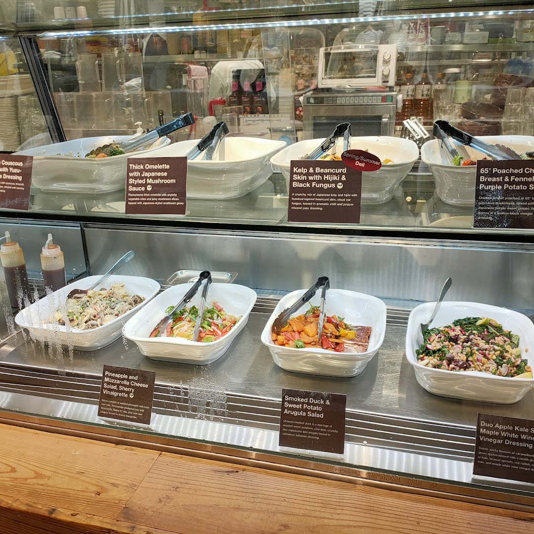 A vibrant display of fresh salads and prepared dishes in a deli counter at CafèMeal.