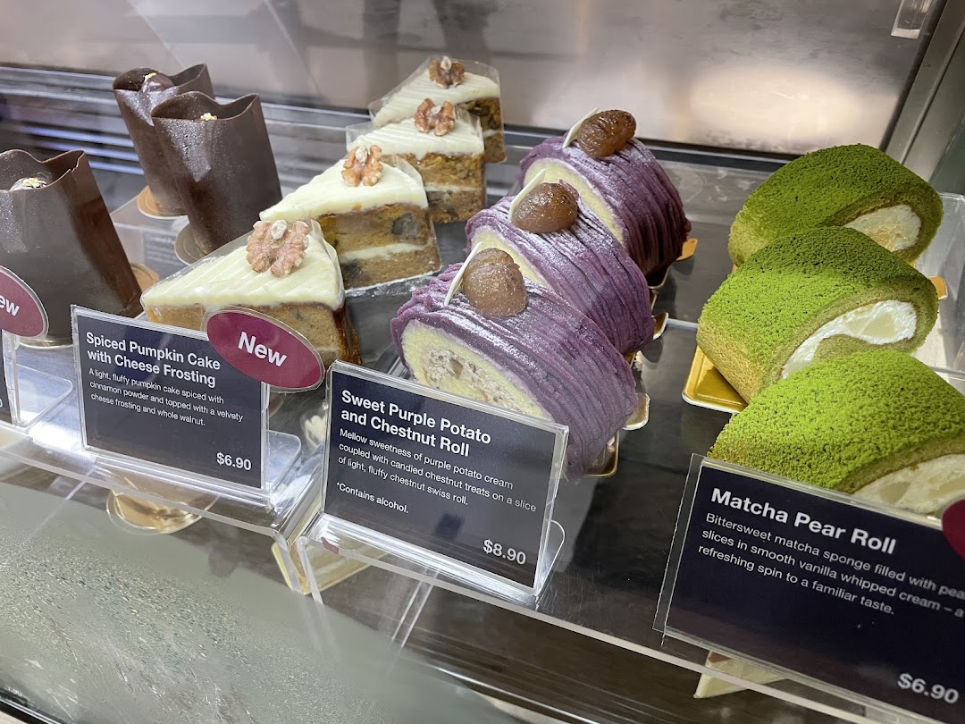 A vibrant display of delicious cakes and pastries, including pumpkin, purple potato, and matcha flavors, with prices.