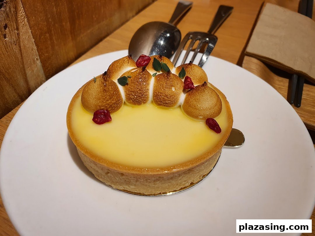 A close-up of a delicious lemon meringue tart with toasted meringue peaks and red berry garnish.