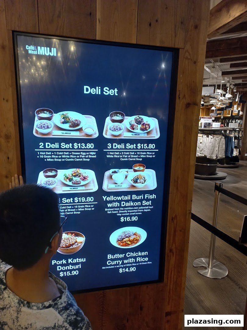 A child views a digital menu board at CafèMeal MUJI, showcasing various deli sets and Japanese-inspired dishes.