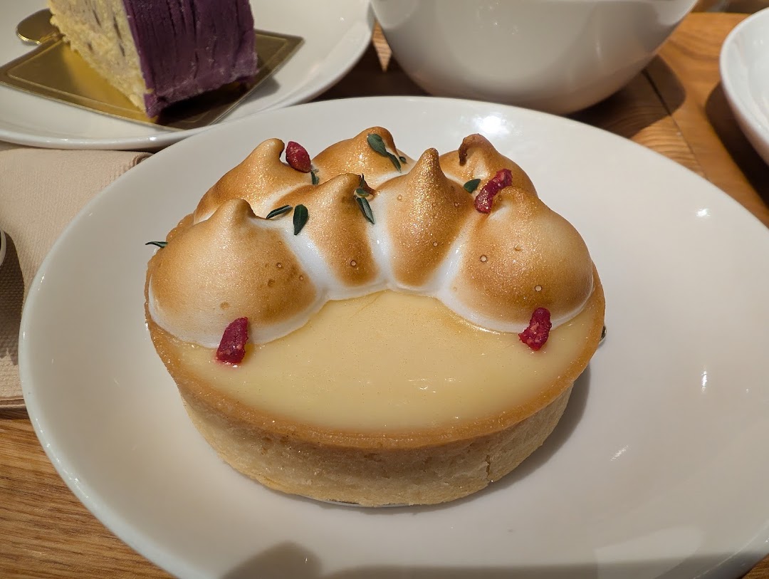A close-up of a beautifully presented lemon meringue tart with golden meringue and red sprinkles.