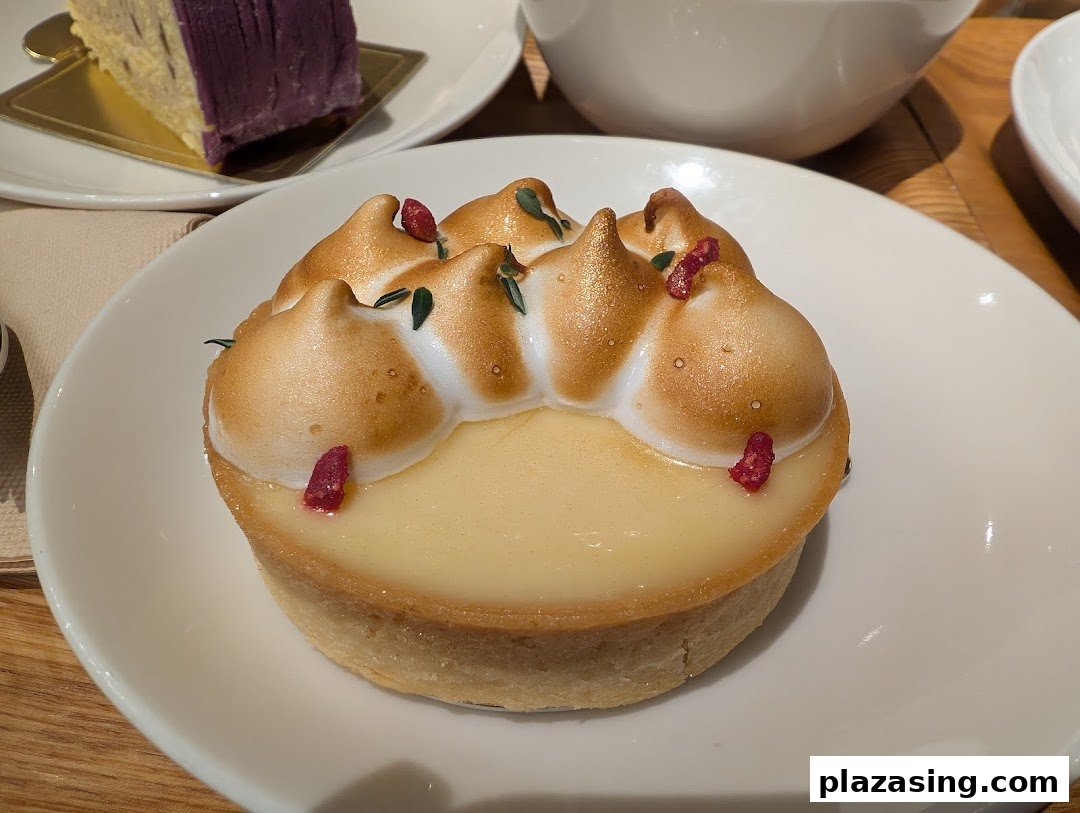 A close-up of a beautifully presented lemon meringue tart with golden meringue and red sprinkles.