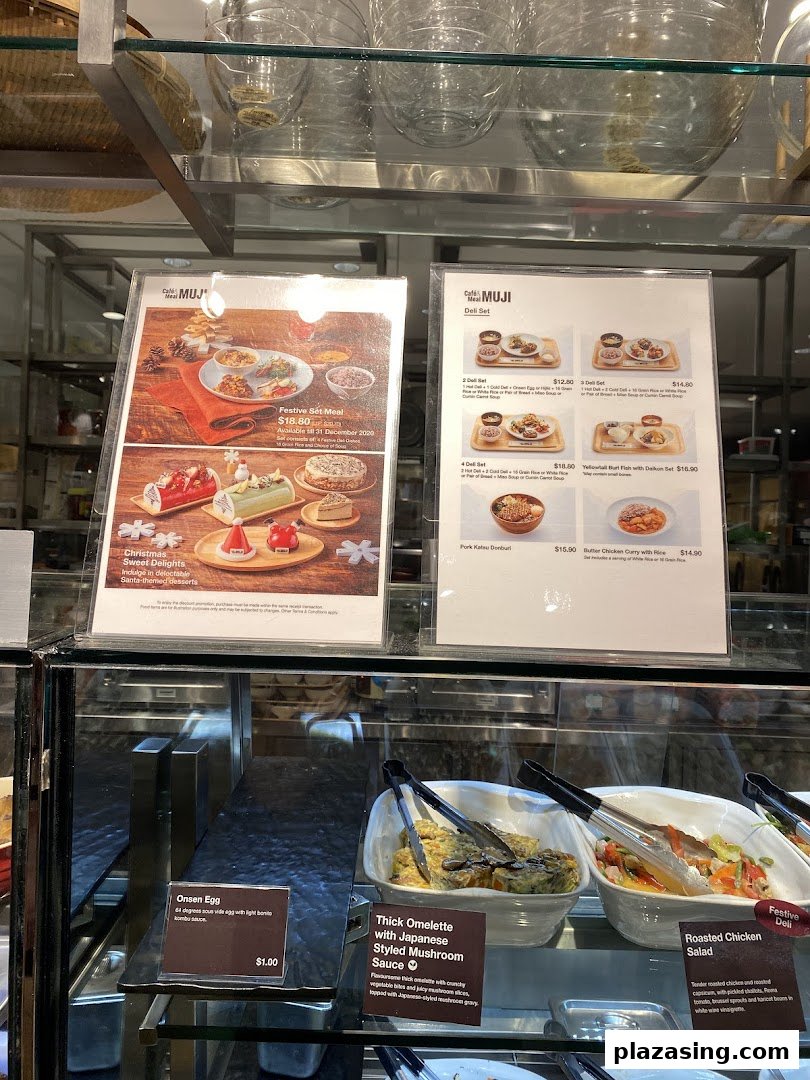 An interior view of CafèMeal MUJI, showcasing menu boards with festive specials and deli sets, alongside prepared food items.