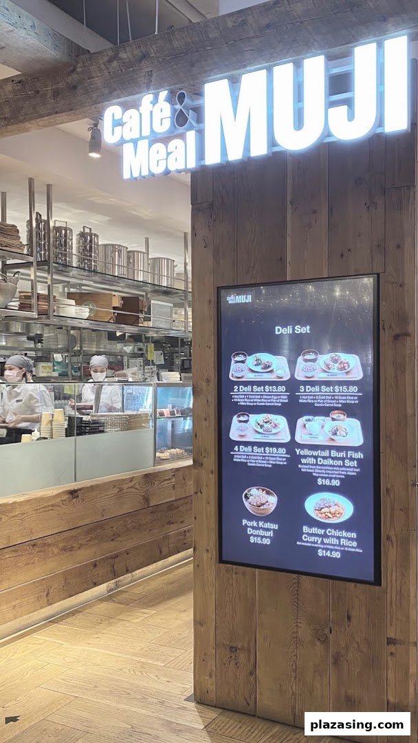 The entrance of Café & Meal MUJI featuring a digital menu board displaying various deli sets and main dishes.