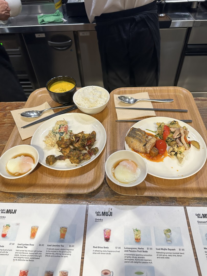 Two wholesome meal trays with various dishes, including rice, soup, and main courses, in a cafe setting with a partial menu visible.