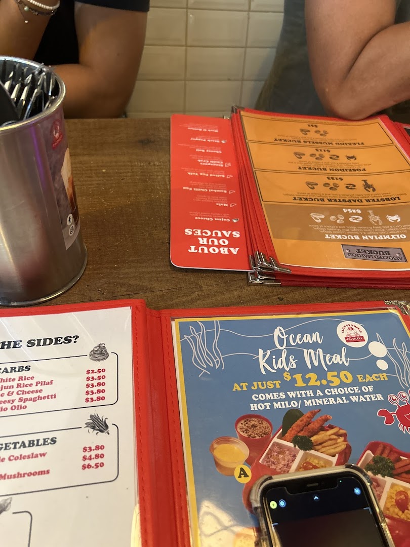 A close-up view of open menus on a wooden table, showcasing various seafood buckets, sides, sauces, and a kids' meal.
