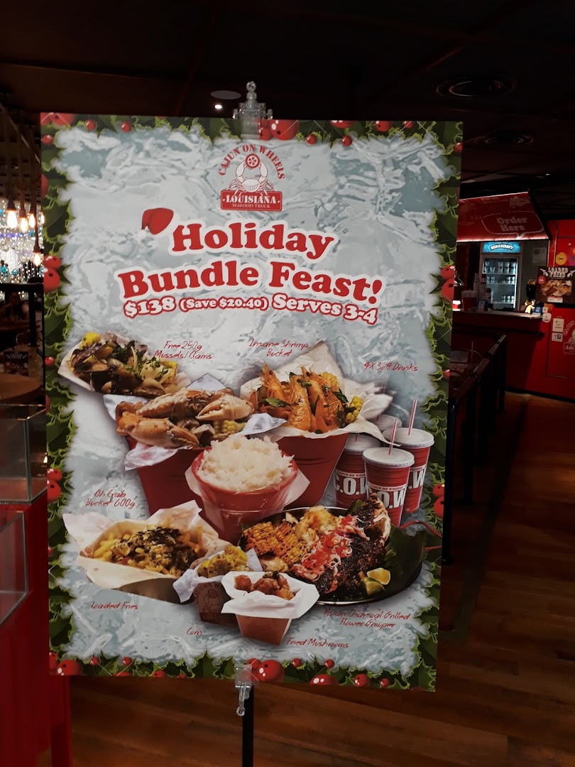A promotional standee for Cajun on Wheels' 'Holiday Bundle Feast' featuring various seafood dishes.