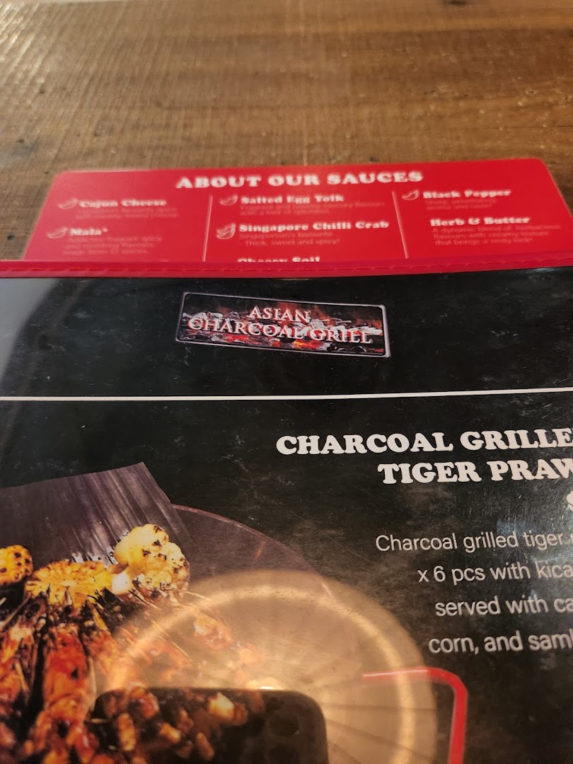 A close-up of a menu displaying various sauce options and a charcoal-grilled tiger prawn dish.