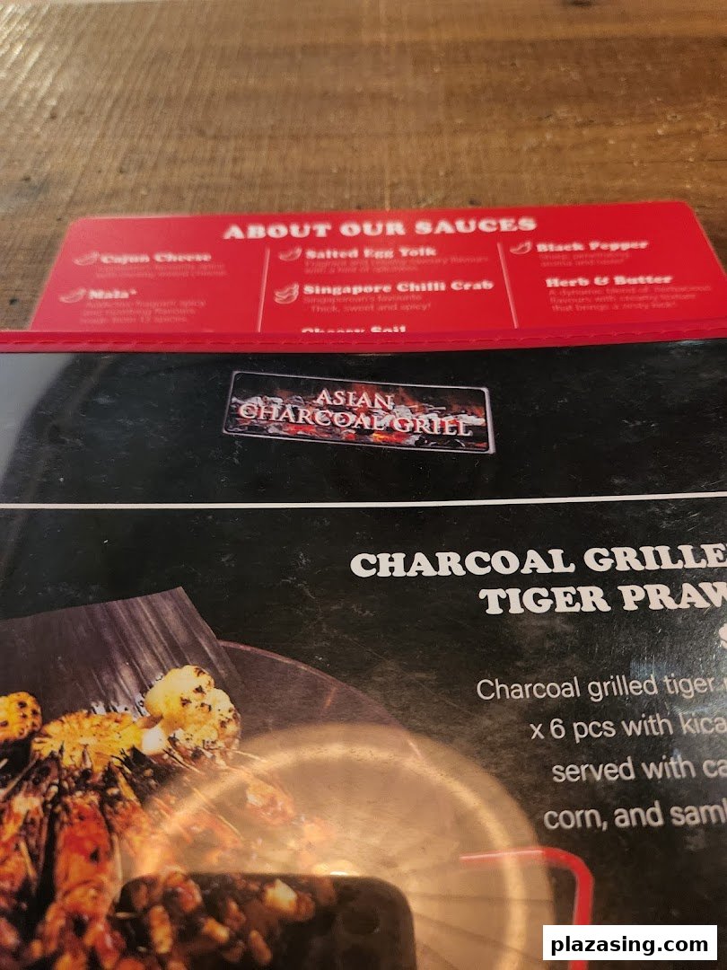 A close-up of a menu displaying various sauce options and a charcoal-grilled tiger prawn dish.