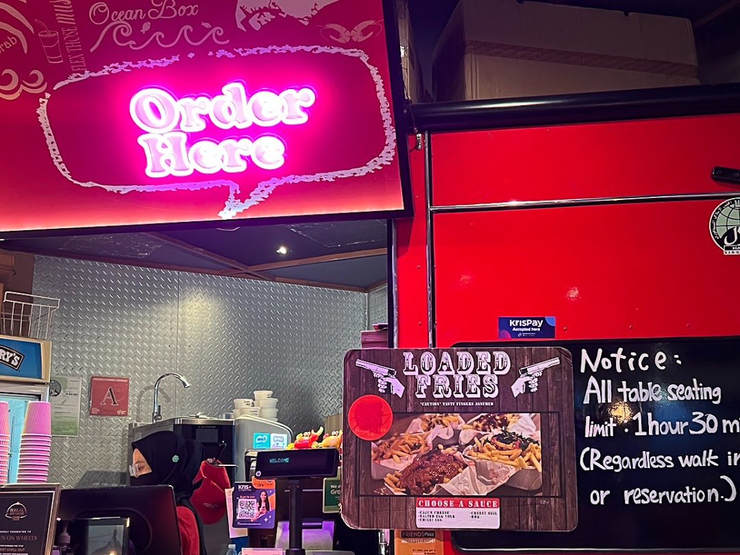 A vibrant counter at Cajun on Wheels, featuring a neon 'Order Here' sign and a 'Loaded Fries' display.
