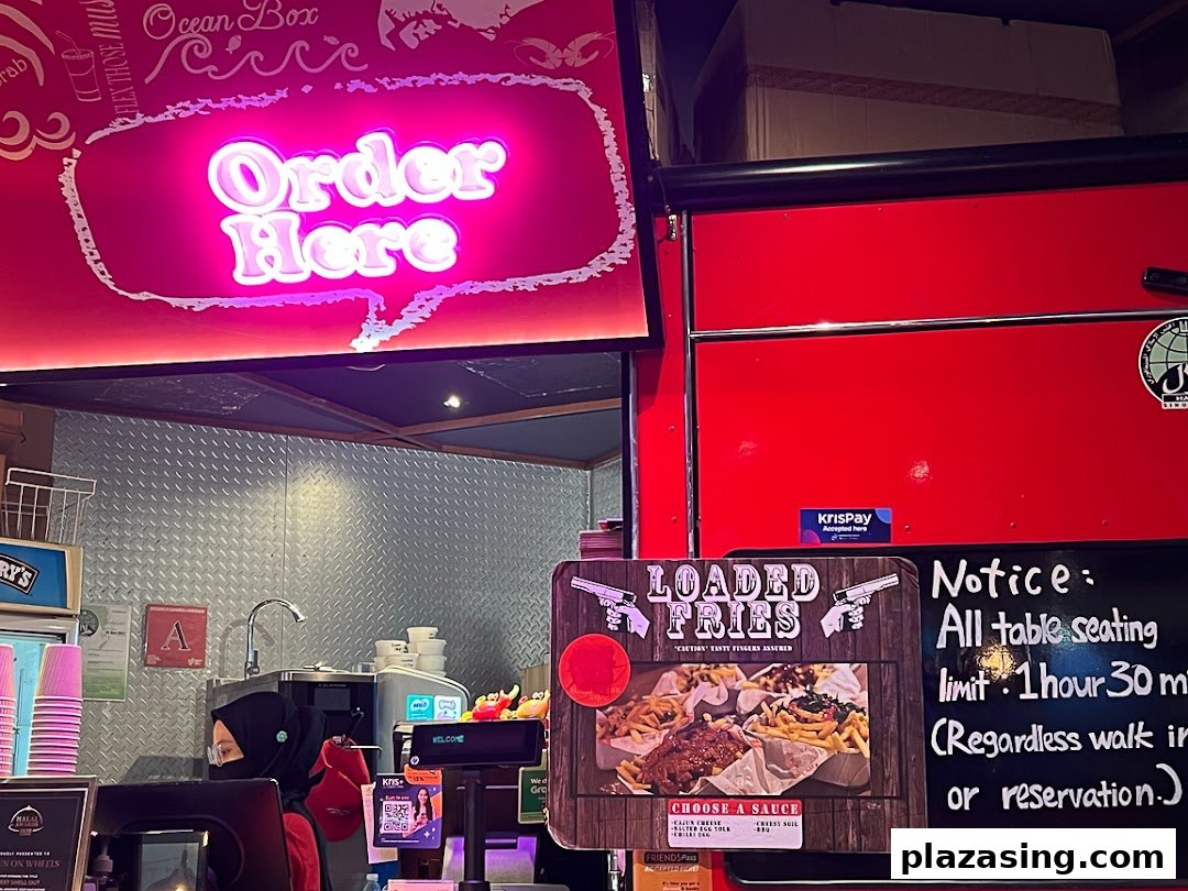 A vibrant counter at Cajun on Wheels, featuring a neon 'Order Here' sign and a 'Loaded Fries' display.