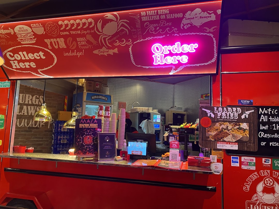 A vibrant food stall counter with neon 'Order Here' sign, showcasing Cajun-inspired seafood and fries.