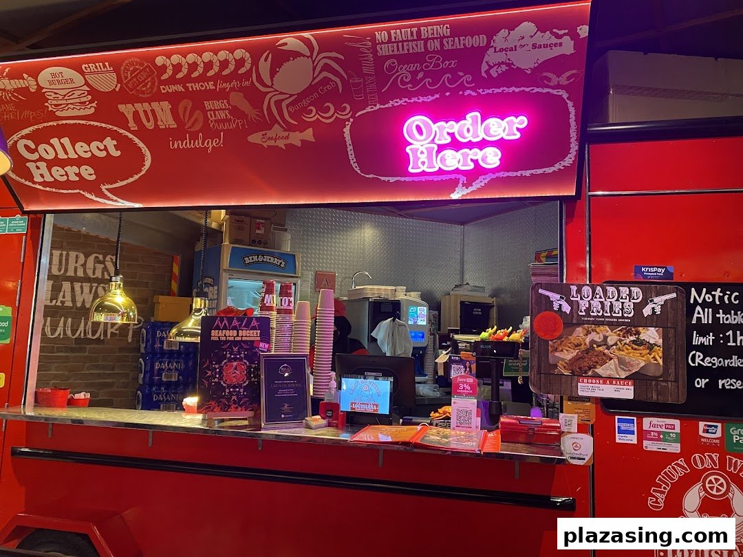 A vibrant food stall counter with neon 'Order Here' sign, showcasing Cajun-inspired seafood and fries.