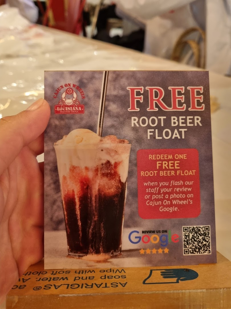 A hand holds a promotional card for Cajun on Wheels offering a free root beer float.