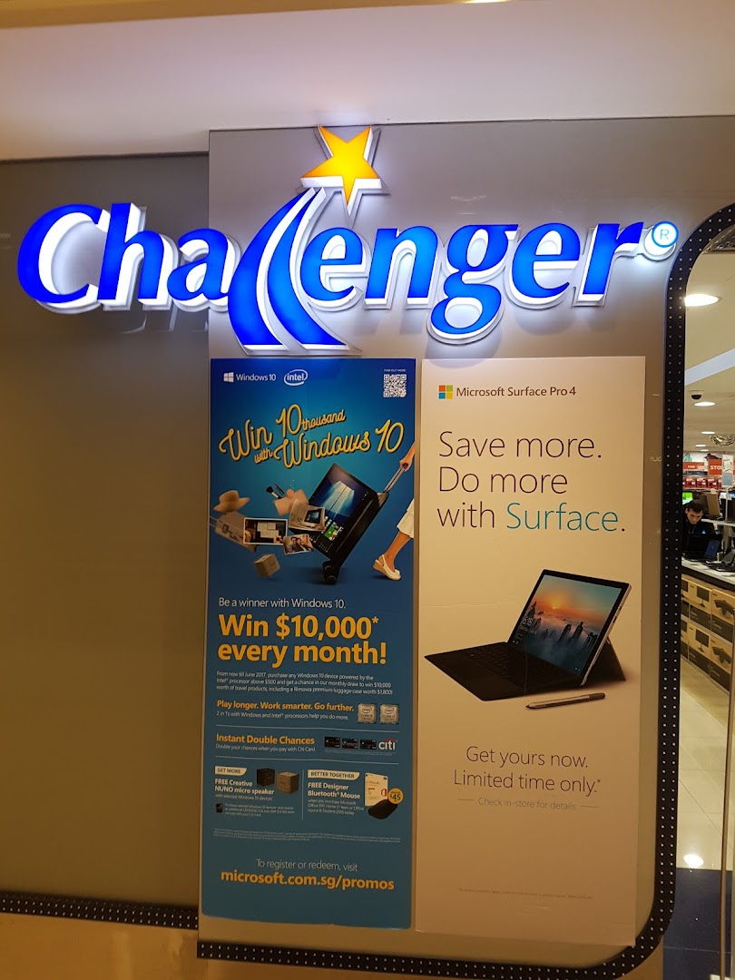 Challenger electronics store front with illuminated logo and promotional posters for Windows 10 and Microsoft Surface.